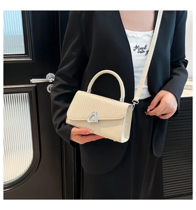 Detail of beige woven handbag featuring a heart metal lock and stylish stitching accents
