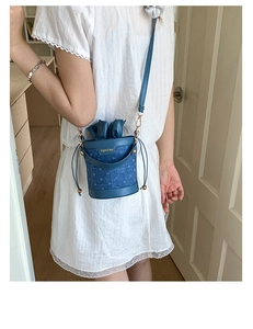 Detail of blue textured bucket bag featuring drawstring closure and gold hardware