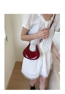 Red patent leather half-moon shoulder bag with gold hardware worn by model