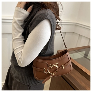 Detailed view of warm brown leather bag with a stylish gold bow metal accent on the front