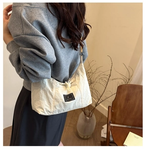Detail of a minimalist white pleated tote bag with drawstring closure and brand label