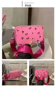 Detailed view of pink PU leather crossbody bag featuring red cherry prints and wide strap