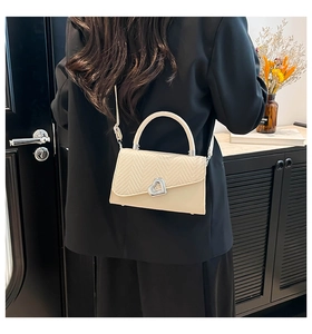 Detail of cream crossbody bag featuring woven texture flap and silver heart rotary buckle