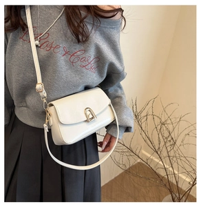 Gros plan d'un sac bandoulière rectangulaire crème avec boucle dorée et bandoulière réglable