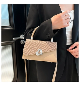 Detail showing the beige woven textured bag with a silver heart-shaped twist lock closure