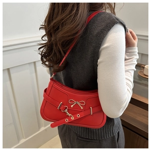 Detail of red faux leather shoulder bag featuring metal bow and buckle on the back of model