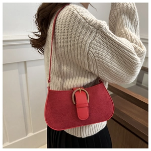 Detail of red suede underarm bag with gold metal buckle on a shoulder-worn model