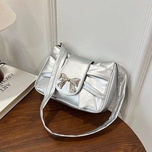 Silver metallic bow handbag with wide strap on a wooden table, 2025 summer fashion style