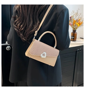 Detail of elegant beige crossbody bag with woven flap and heart-shaped silver lock