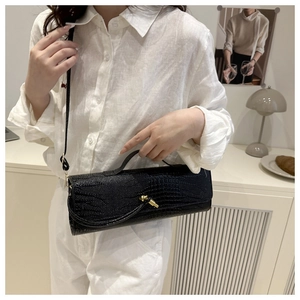 Detail of black crocodile pattern handbag with gold knot hardware and crossbody strap