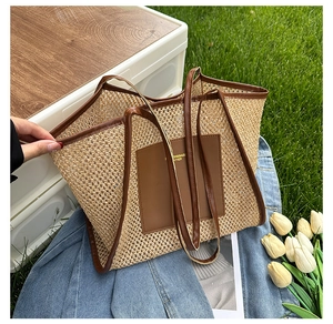 Close-up of woven straw tote bag with brown leather trim and pocket on denim background