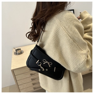 Detail of black underarm bag with gold bow ornament on shoulder strap