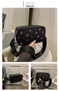 Detail of black crossbody bag with red cherry print, double zipper, and wide nylon strap