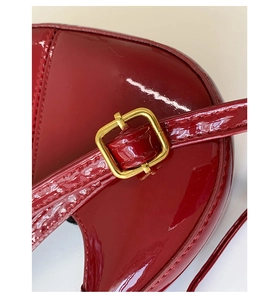 Détail rapproché d'un sac à bandoulière en cuir verni rouge brillant et boucle dorée