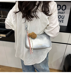 Detail view of silver leather underarm bag with cute teddy bear and ribbon charms