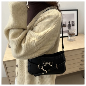 Détail d'un sac à bandoulière en cuir noir brillant avec boucle nœud dorée et ceinture à œillets