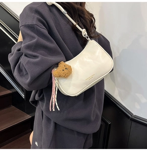 Detail of a creamy white crescent bag with brown plush bear charm and woven rope accent