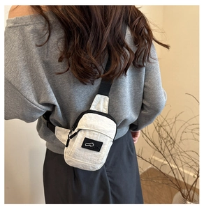 Detail of white nylon crossbody bag with black adjustable strap and decorative patch