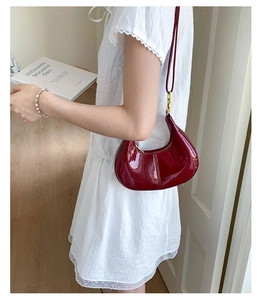 Close-up of glossy burgundy patent leather shoulder bag with gold hardware on white dress