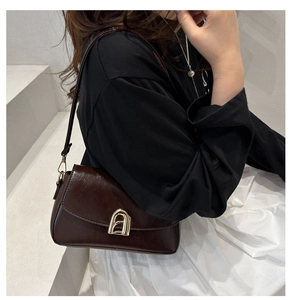 Détail d'un sac à bandoulière en cuir marron foncé avec boucle dorée sur modèle