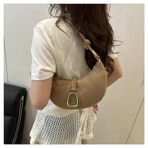 Detail of tan woven crescent bag with gold horseshoe buckle and knotted shoulder strap