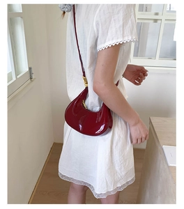 Model wearing a deep burgundy crescent bag in glossy patent leather with gold hardware