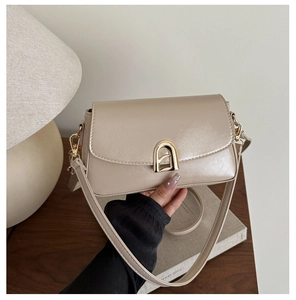 Détail de la sacoche beige montrant la boucle dorée en arche et la texture du cuir