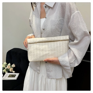 Dettaglio di una pochette in paglia beige con strisce testurizzate e borchie dorate
