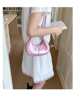 Pink glossy patent leather hobo bag held by a model in a stylish indoor setting