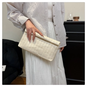 Detail of hand-woven minimalist straw clutch bag held by model for summer beach style