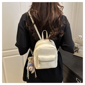 Nahaufnahme des cremefarbenen Mini-Rucksacks mit Plüschbären-Anhänger und mattem Leder