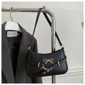 Détail du sac porté épaule noir en similicuir avec boucle nœud doré sur un blazer
