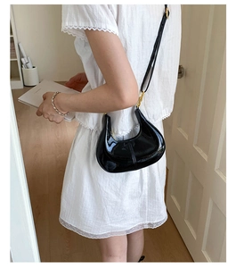 Detail of a black patent leather half-moon crossbody bag with golden hardware and strap
