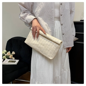 Detail of elegant beige woven straw clutch bag with textured wave pattern held by model