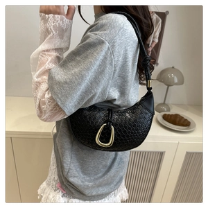 Detail of woven black crescent shoulder bag with golden ring and knotted strap