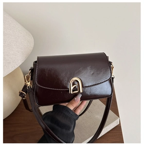 Détail de la texture en cuir verni marron foncé et de la boucle en fer à cheval dorée