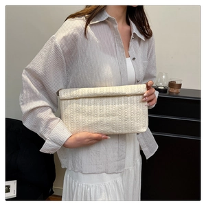 Detail of cream woven clutch bag with metal clasp closure on striped shirt background