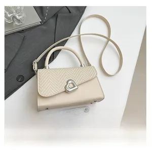 Detail of cream crossbody bag with heart lock beside phone for size reference