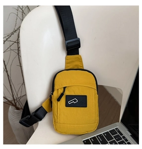 Detail of a bright yellow waterproof nylon chest bag with adjustable black strap on a chair