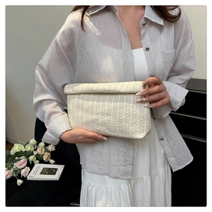 Detail of hand-held beige woven envelope clutch bag with textured pattern and metal buckle