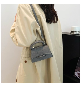 Sac à main sablier gris avec base incurvée et fine bandoulière porté sur un trench beige