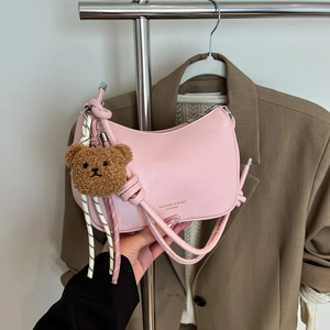 Pink crescent shoulder bag with knotted strap and teddy bear charm on model