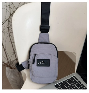Detail showing the gray nylon sports crossbody bag with MX logo on a modern chair