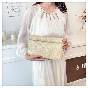 Detail of hand-woven straw envelope clutch bag held by model wearing a white dress