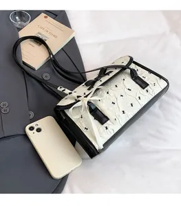 Detail of elegant white pleated shoulder bag with black bow embroidery and leather strap