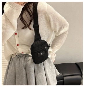 Détail de la sacoche en nylon noir avec sangle réglable et logo sur fond de mur blanc