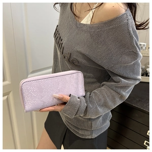 Close-up of lilac embossed leather long wallet held by a model in casual grey knitwear