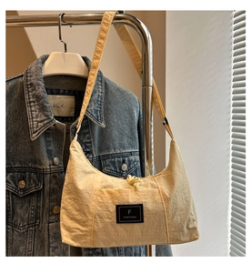 Detail of minimalist cream crescent hobo bag with nylon texture and black woven brand label