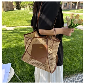 Detail of woven straw tote bag featuring leather handles and brand logo patch outdoors