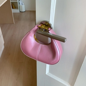 Détail du sac demi-lune en cuir verni rose avec fermeture éclair dorée sur une porte